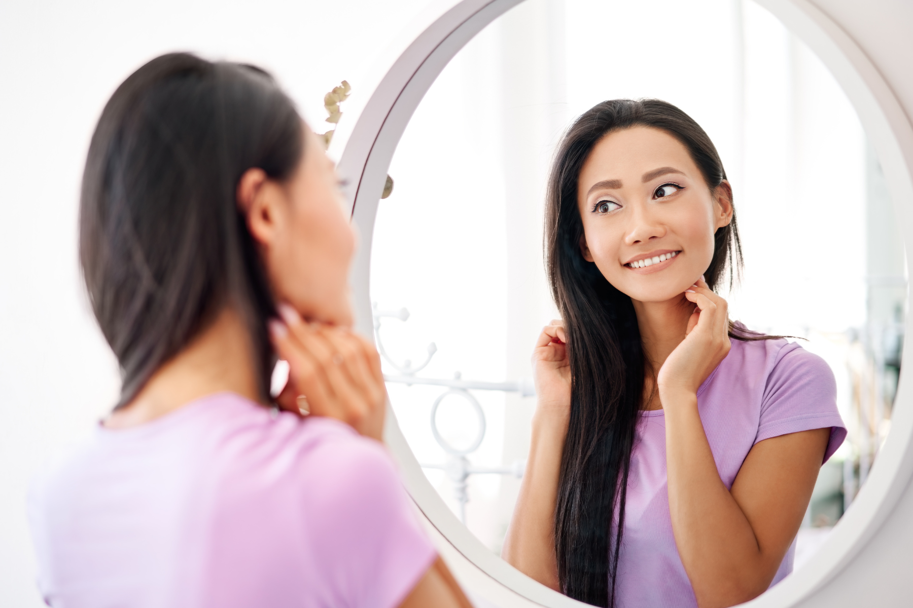 Woman looking at herself in a mirror on a vanity, smiling.