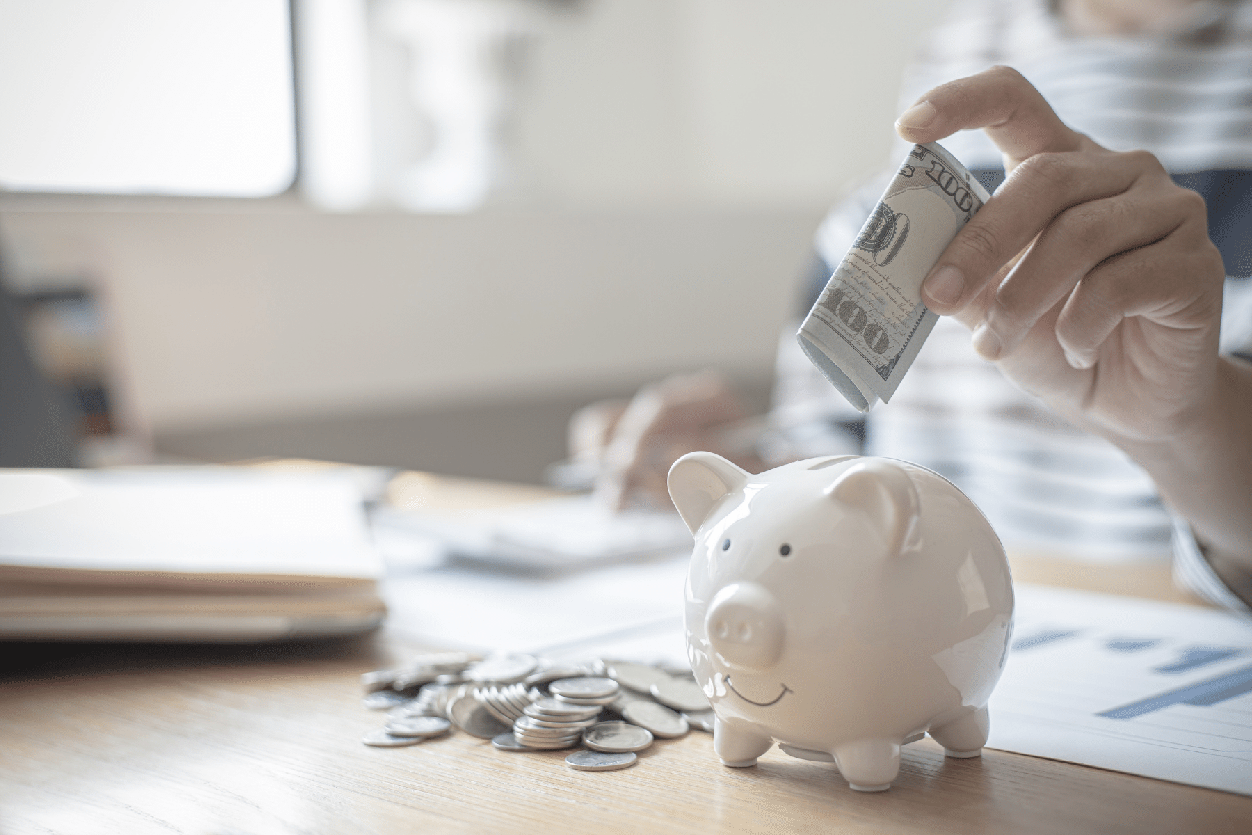 A close up of someone putting money in a clear piggy bank.