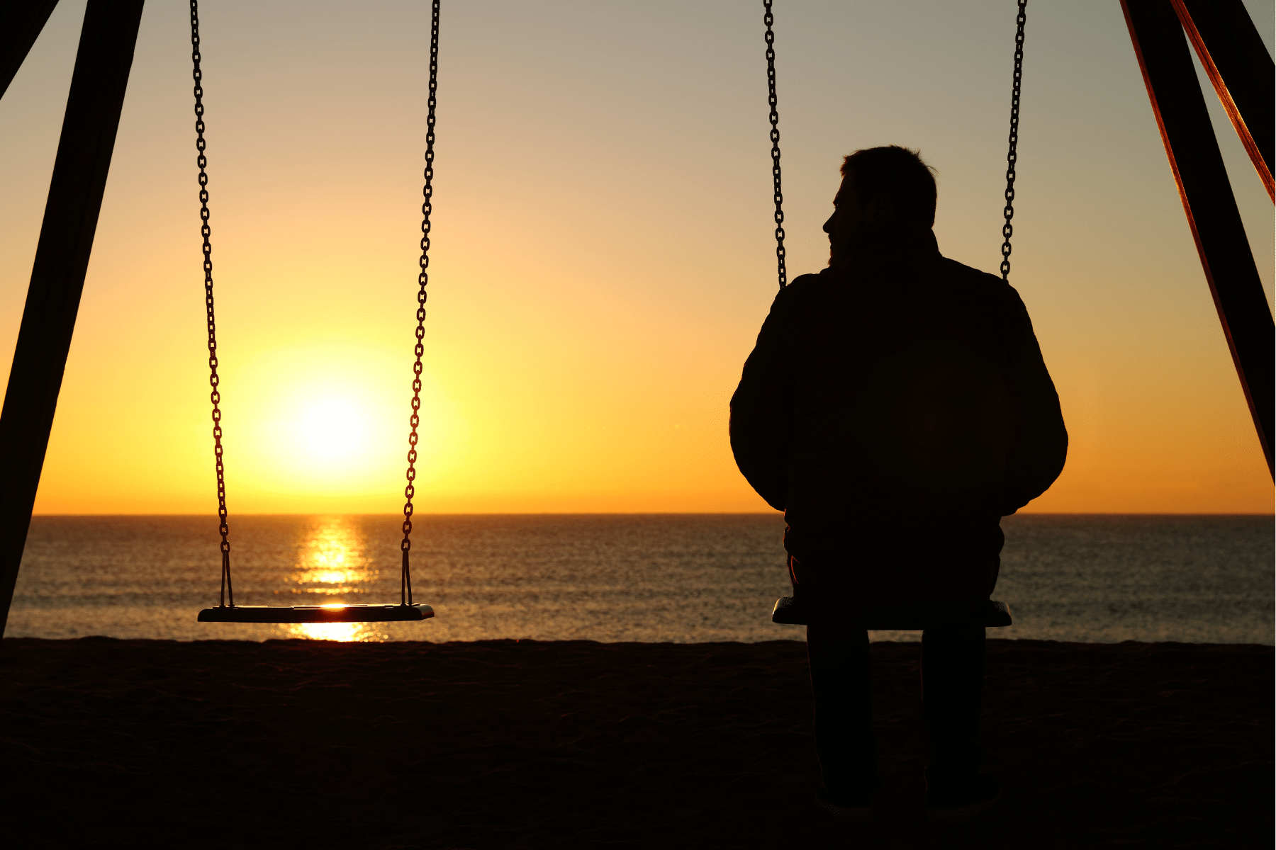 picture of a person sitting on a swing next to an empty seat while looking at the sunset.