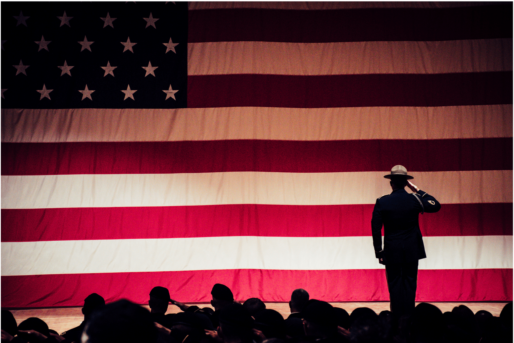 Silhouette of a soldier standing in front of an American flag an saluting.