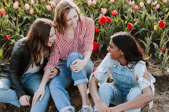 Three young women sitting outside laughing together near flowers